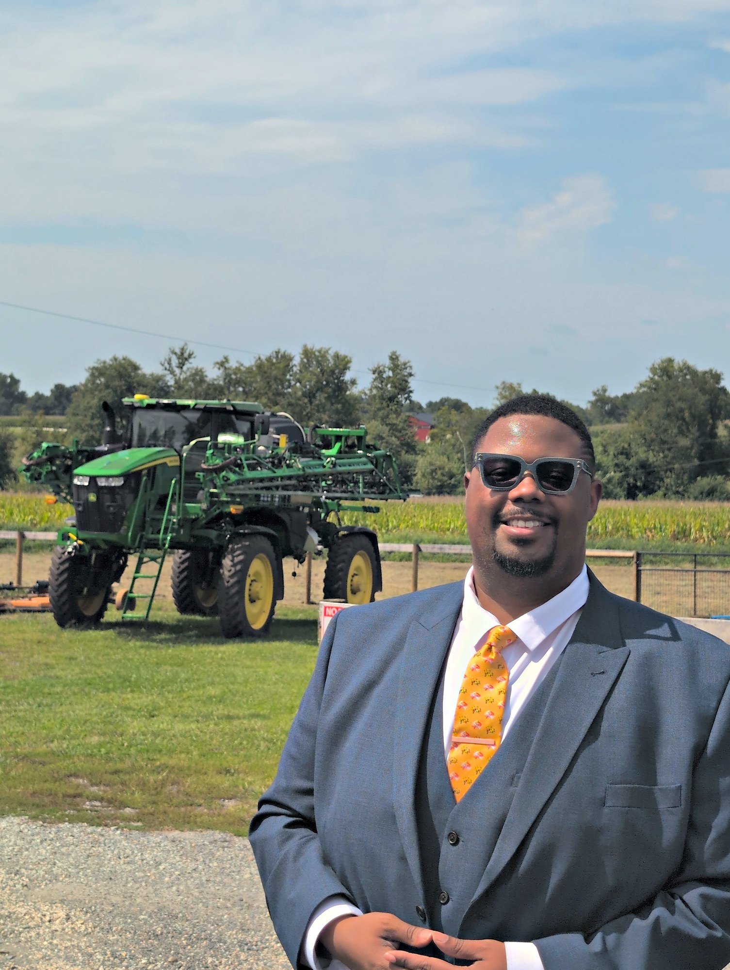 Michael Eckels Jr., candidate for Maryland House of Delegates District 35A, in a blue suit beside a green sprayer on a working farm in Harford County